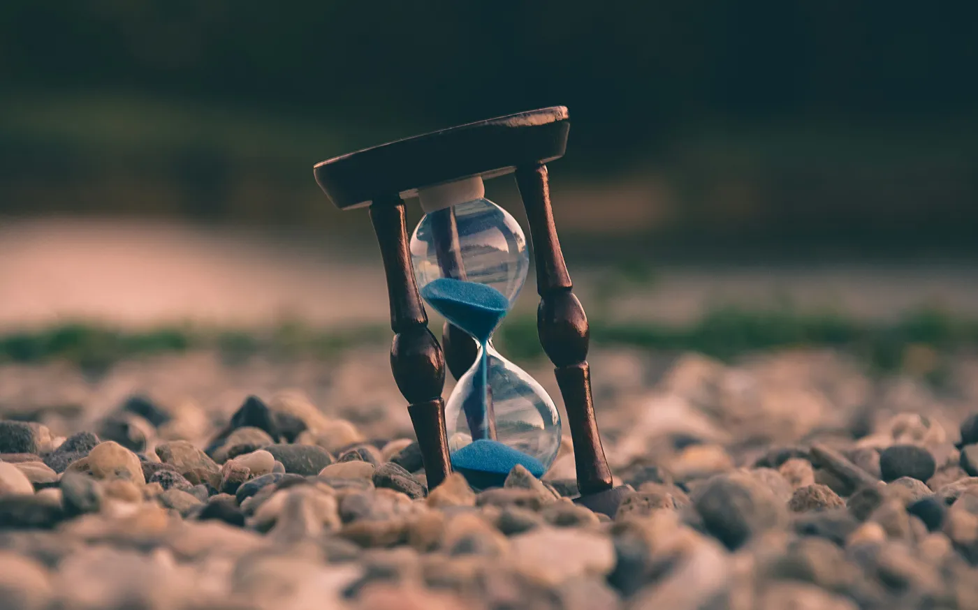 selective focus photo of brown and blue hourglass on stones by Aron Visuals courtesy of Unsplash.